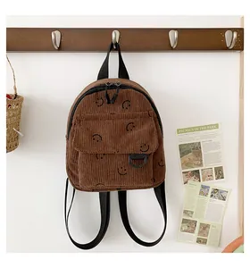 Detailed texture of brown corduroy backpack featuring black smiley face prints on hooks