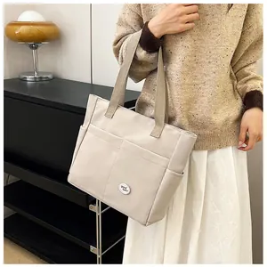 Close-up of beige canvas tote bag featuring front pockets and good luck badge detail