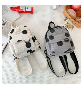 Detail view of mini corduroy backpacks in cream and gray with black polka dots patterns
