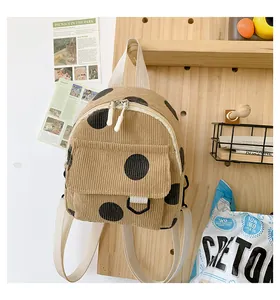 Detail of corduroy mini backpack featuring khaki fabric and black polka dots with dual zippers