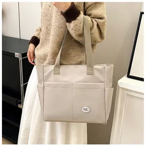 Detailed close-up of beige canvas tote bag featuring double front pockets and patch
