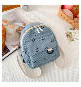 Close-up of blue corduroy backpack featuring a smiley face and front flap pocket detail