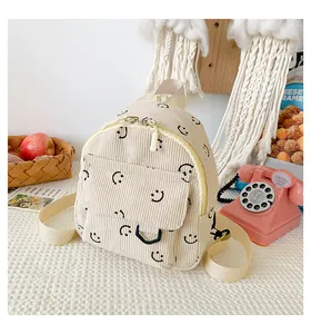 Detail of cream corduroy mini backpack featuring repeat black smiley face patterns