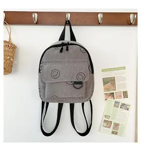 Close-up of grey corduroy backpack featuring black smiley face prints and front pocket