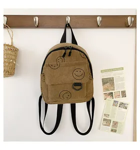 Brown corduroy backpack with smiley prints hanging on a wooden wall hook in a room