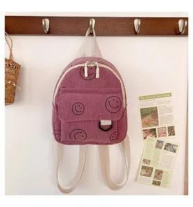 Detail of mauve corduroy mini backpack with black smiley face pattern and white straps
