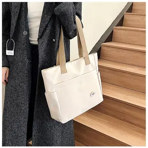 Close-up of cream canvas tote bag featuring front pockets and good luck patch detail