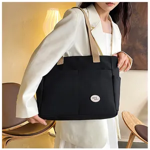 Detail view of a large black canvas tote bag showing multiple pockets and good luck patch
