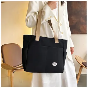 Detail of black canvas tote bag with good luck patch and khaki straps on model