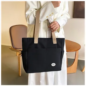 Detail of a black canvas tote bag showing outer pockets and a good luck patch detail
