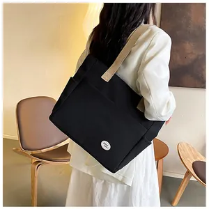 Detailed view of black canvas tote bag featuring front pockets and good luck emblem