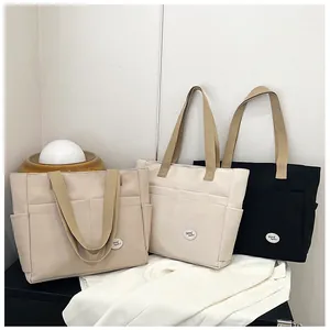 Detail view of khaki, off-white, and black canvas tote bags with good luck patch