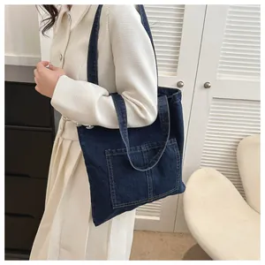 Detailed shot of a navy denim tote bag with large front pocket on a fashion model