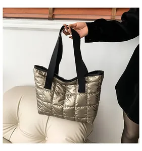 Detail einer gesteppten Daunentasche in Gold mit Metallic-Finish und schwarzen Griffen