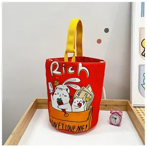 Detail view of red canvas bucket bag with cartoon cats and thick yellow handles on wood tray