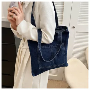 Detail of blue denim tote bag with dual front pockets and contrast stitching on a model