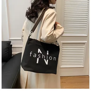 Detail of black canvas tote bag featuring white fashion print and a brown wide shoulder strap
