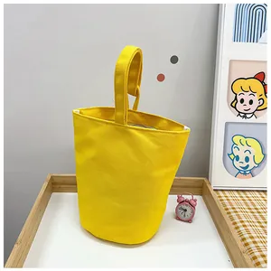 Detail view of a bright yellow canvas bucket bag with a single wide handle on a wooden tray