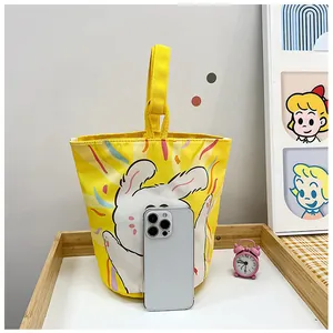Detail of yellow canvas bucket bag with cartoon rabbit print and smartphone for scale