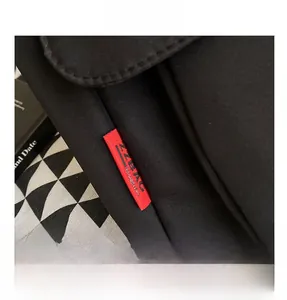 Detail of black fabric messenger bag featuring a red decorative woven label and neat stitching