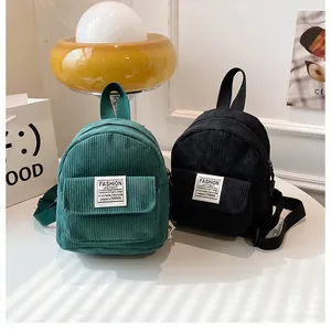 Detail of corduroy mini backpacks in green and black with textured fabric and white labels