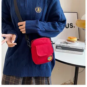 Red canvas crossbody bag shown on model featuring orange embroidery and adjustable strap