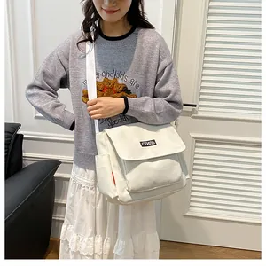 On-body view of cream canvas messenger bag with flap closure and black woven style label