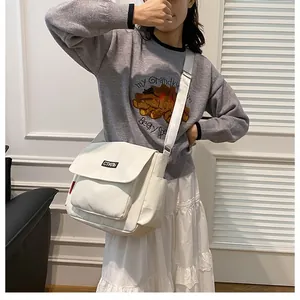Detailed view of the off-white canvas messenger bag featuring a wide strap and side pockets