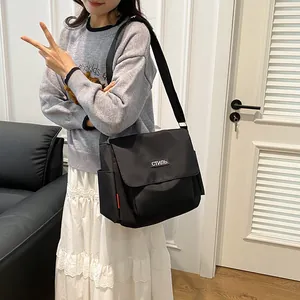 Minimalist black nylon messenger bag with white embroidery and adjustable strap
