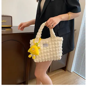 Detail of cream bubble textured handbag featuring a cute yellow plush pendant accessory