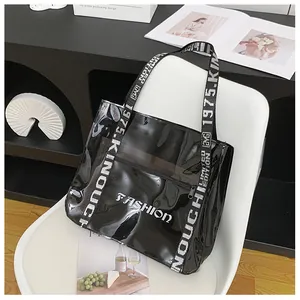 Close-up of black glossy patent leather tote bag with fashion text and branded strap