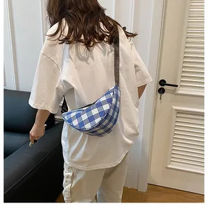 Detail of blue and white checkered crescent bag with adjustable wide black strap on shoulder