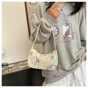 Detail view of a cream shoulder bag featuring bold blue letters and artistic ink splashes