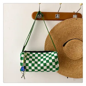Detail of green and white checkerboard barrel bag on a wooden hook with a straw hat