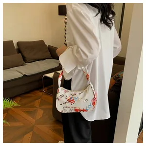 Detail of white half-moon underarm bag with artistic graffiti prints on woman's shoulder