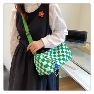 Detail of green and white checkerboard barrel bag with adjustable strap and woven charms