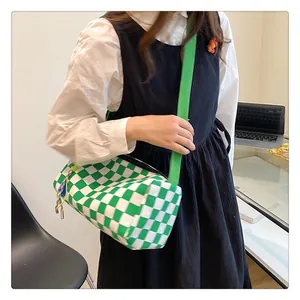 Close-up of green checkerboard canvas crossbody bag with wide shoulder strap on model