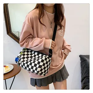 Detail of checkerboard canvas cylinder bag featuring black adjustable shoulder strap