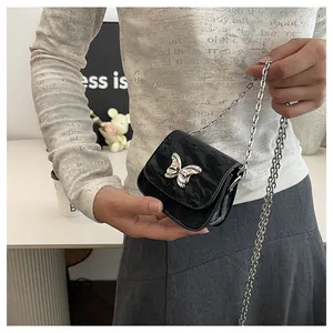 Detail of a black mini crossbody bag with a large silver butterfly buckle and chain strap