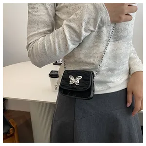 Detail of a black mini crossbody bag with a silver butterfly buckle and chain strap