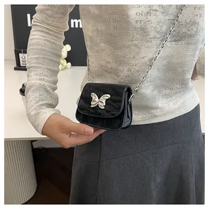 Detail of a black mini crossbody bag featuring a silver metal butterfly and chain strap
