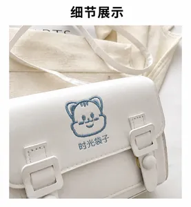 Detail of white PU shoulder bag with blue cartoon cat embroidery and STYNGUET logo