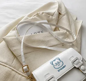 Detail of white PU leather satchel featuring a blue cartoon cat and adjustable strap