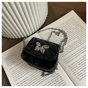 Detail of mini black crossbody bag with silver butterfly clasp and fine chain on a book