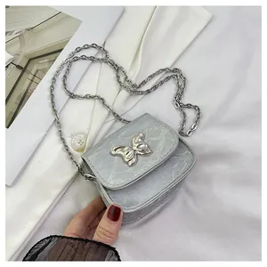 Macro detail of mini silver bow crossbody bag with metallic texture and chain strap