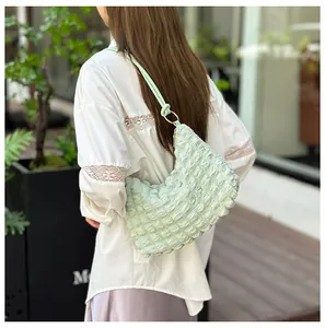 Light green pleated hobo bag with bubble texture shown on a shoulder in a park setting