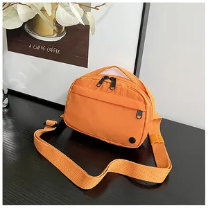 Detail view of an orange nylon crossbody bag on a desk with lifestyle props