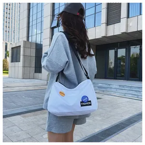 Detalle de bolso medialuna de lona blanca con parches de moda y correa ancha negra