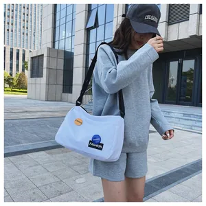 Foto exterior de un gran bolso bandolera de lona blanca con etiquetas de colores vivos