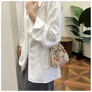 Detail of vintage floral embroidery on small canvas bucket bag with woven drawstring strap